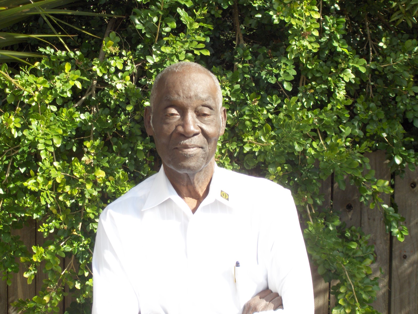 Robert C. Saffold, Sr., standing outdoors in a white shirt, surrounded by greenery.