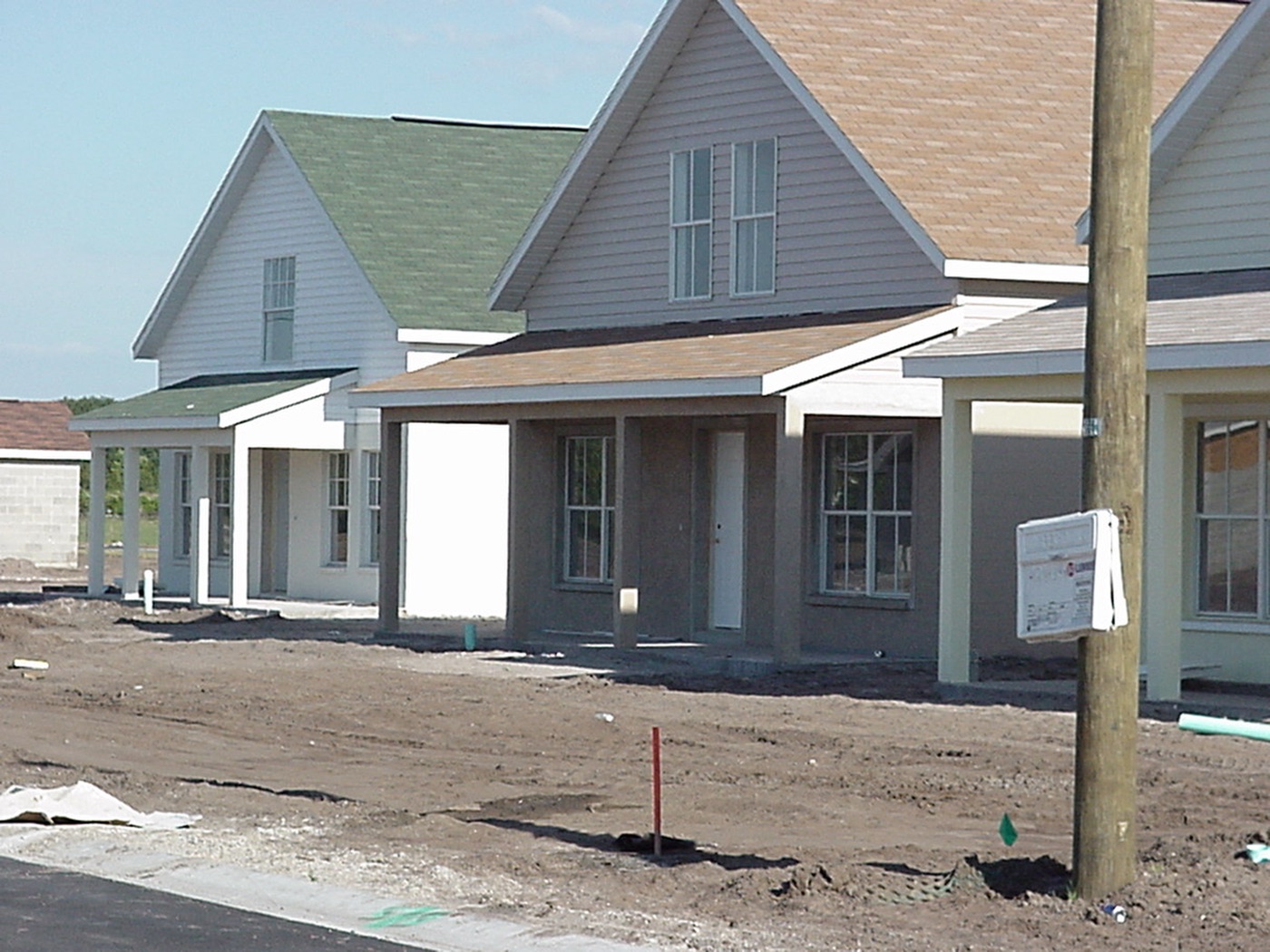 A row of newly framed self-help houses with porches and pale siding standing on a graded lot before landscaping.
